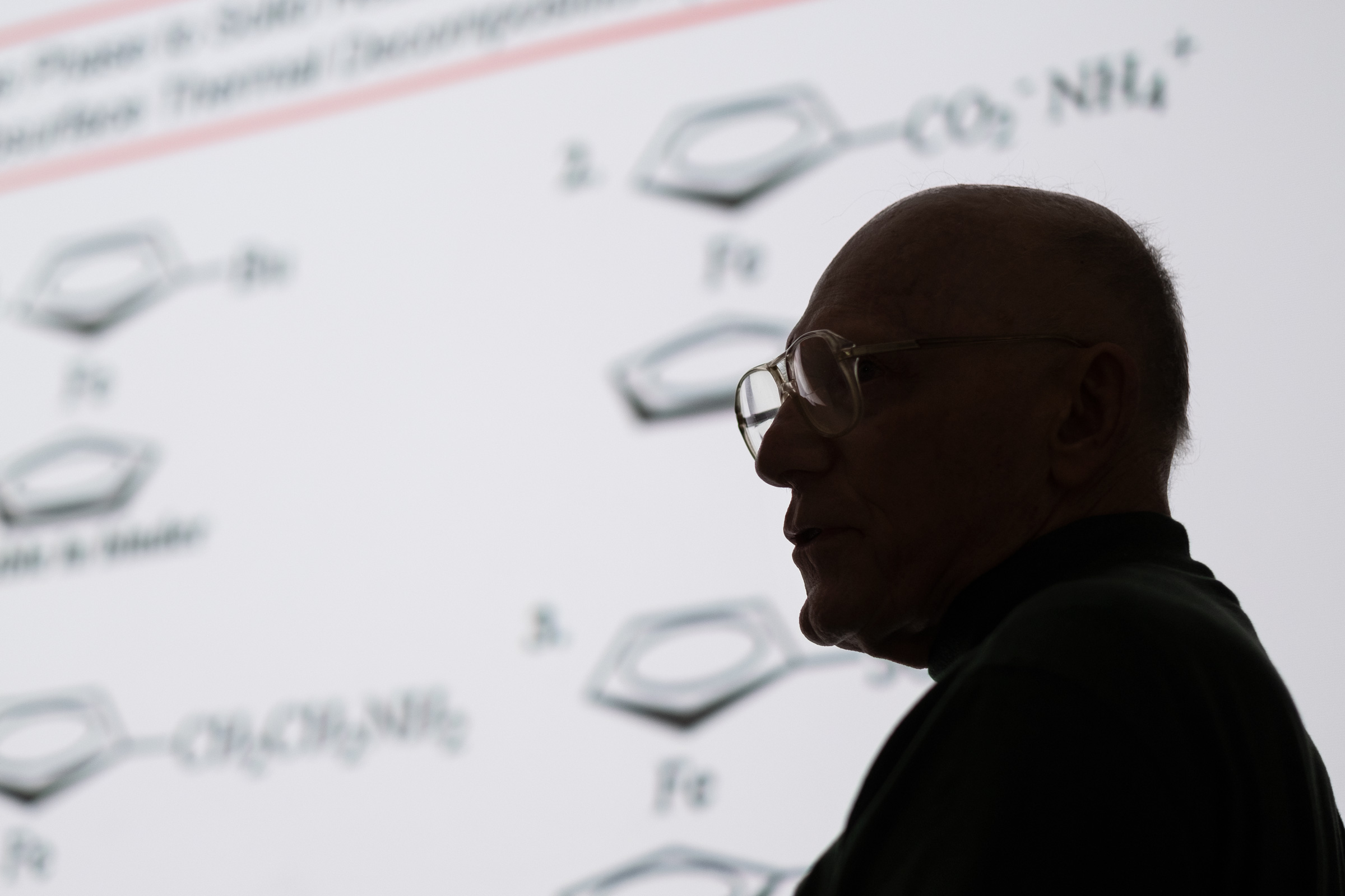 Emeritus Professor Pittman's profile in silhouette with chemistry diagrams projected behind him.