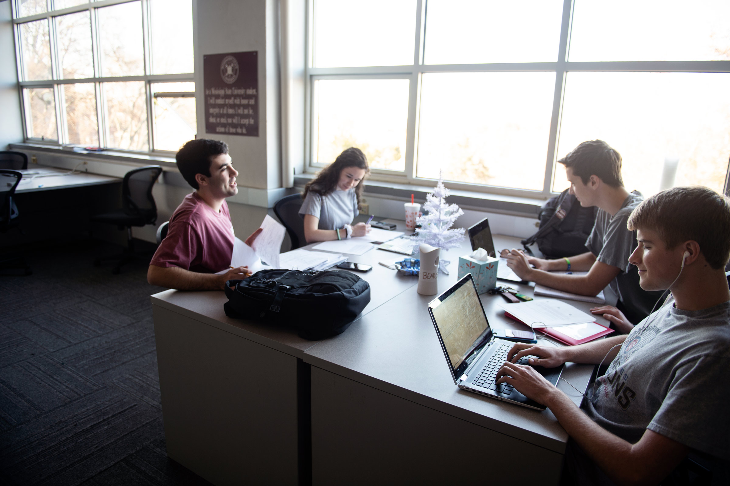 Four geosciences students study for December finals in a Hilbun study lab with a small Christmas tree in the table's center.