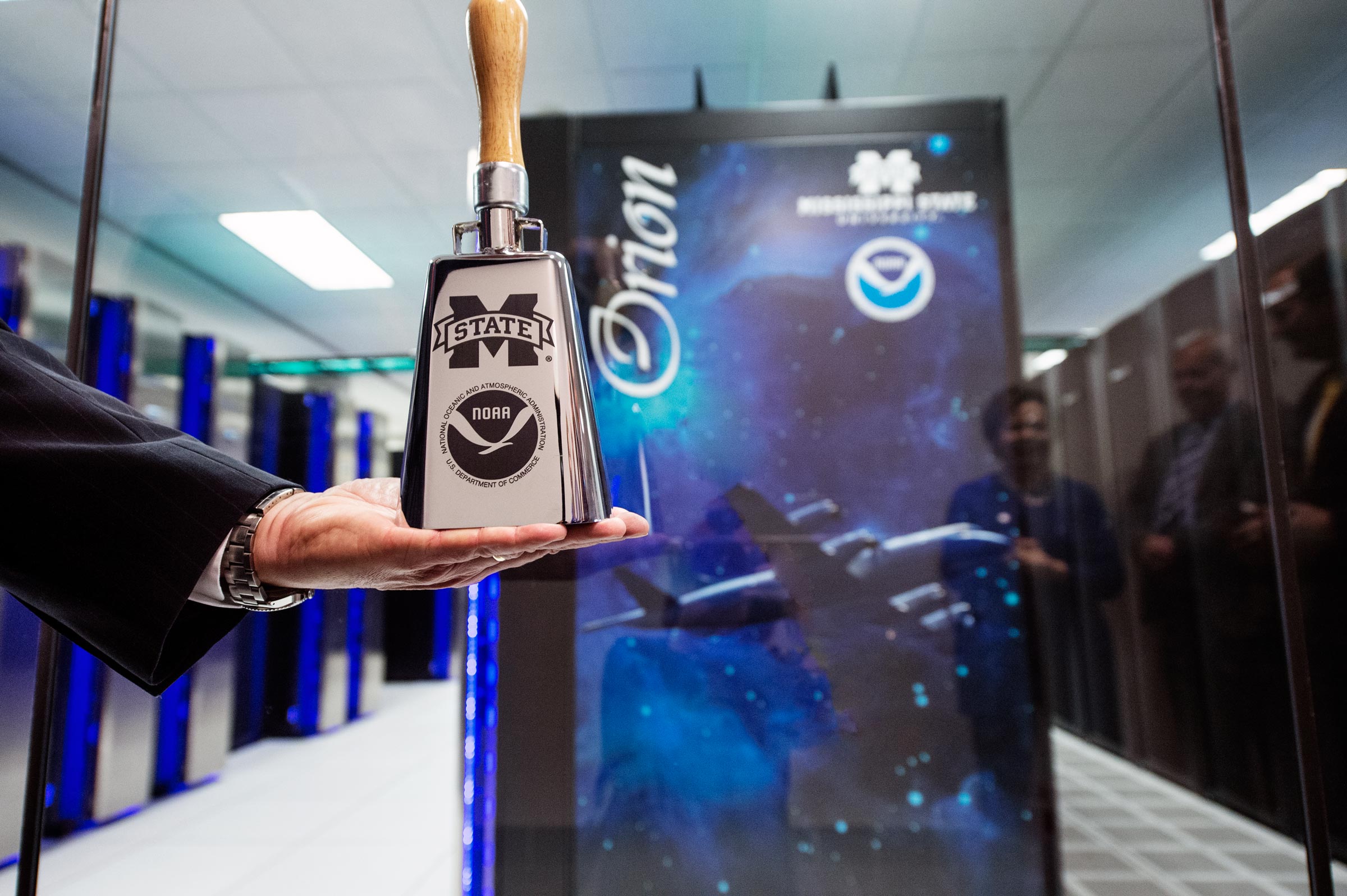 NOAA's Craig McLean holds cowbell in front of Orion supercomputers in HPCC.