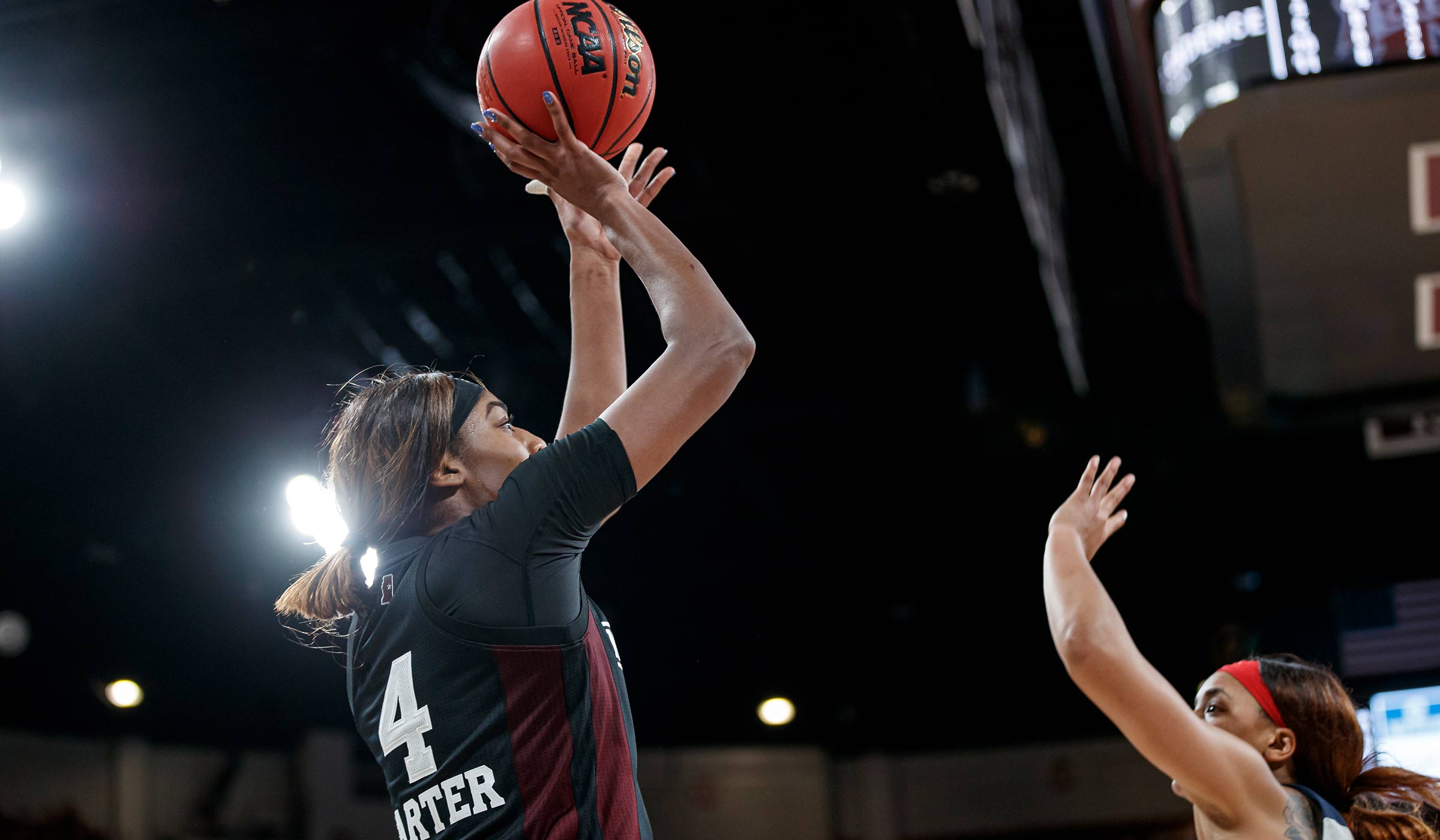 Women's basketball player in black uniform shooting the ball over opponents' head.