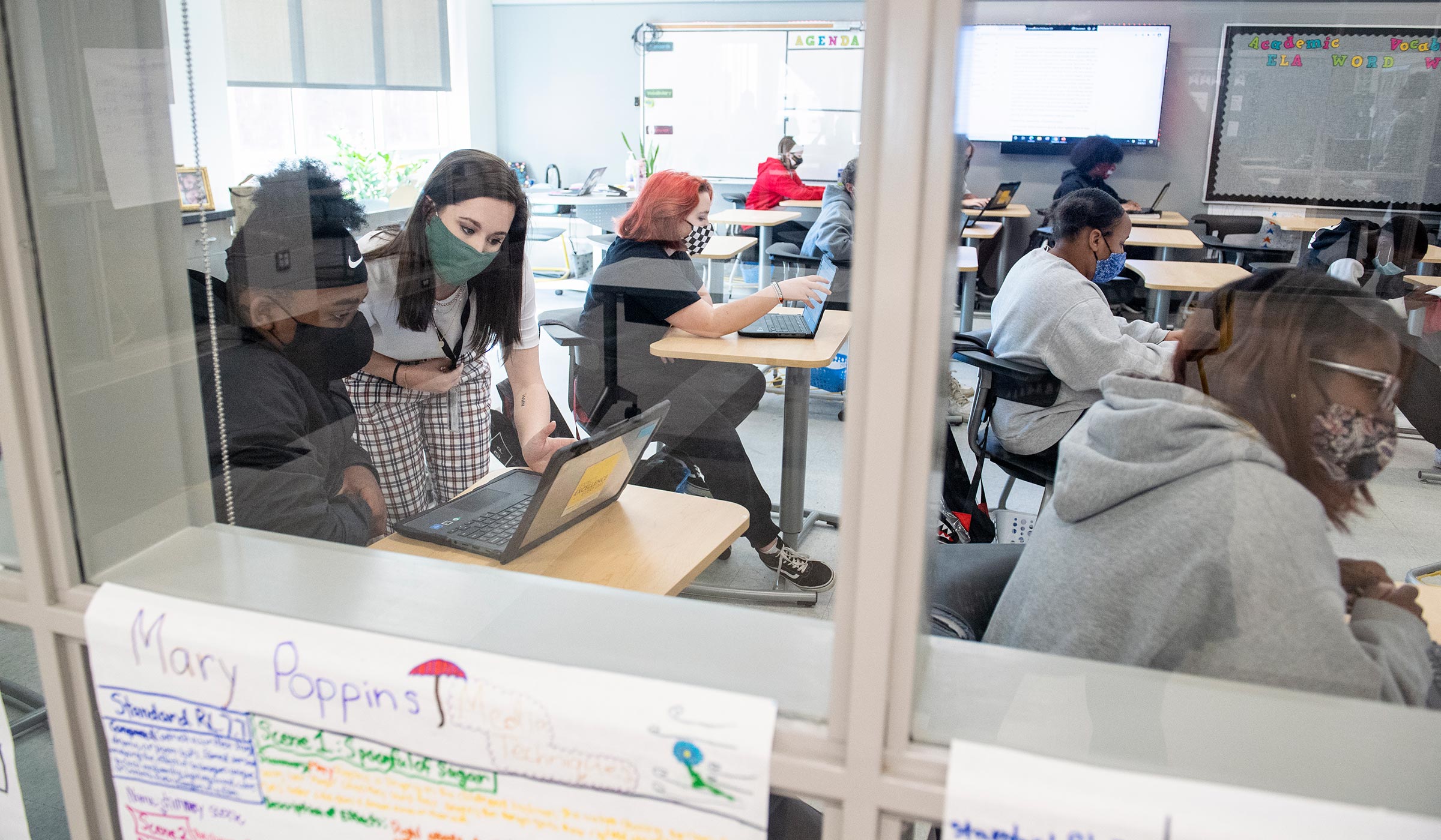 Framed by the windows to the 7th grade classroom, MSU Education major and student teacher Laruen Threadgill bends over a student's desk to provide to provide guidance.