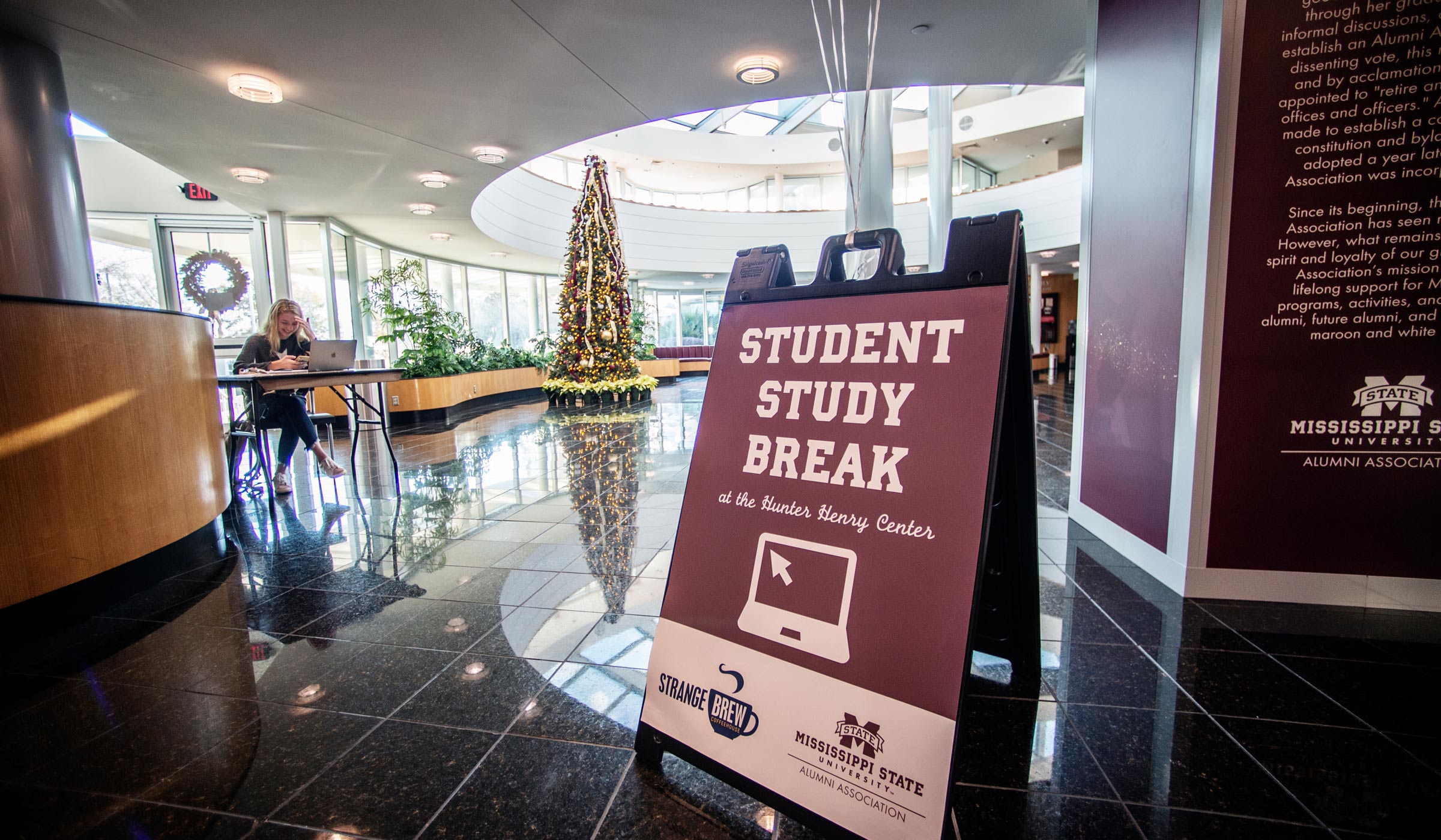 A sign reading "Student Study Break" stands in the foreground, with the Hunter Center Atrium Christmas tree and a studying student beyond.
