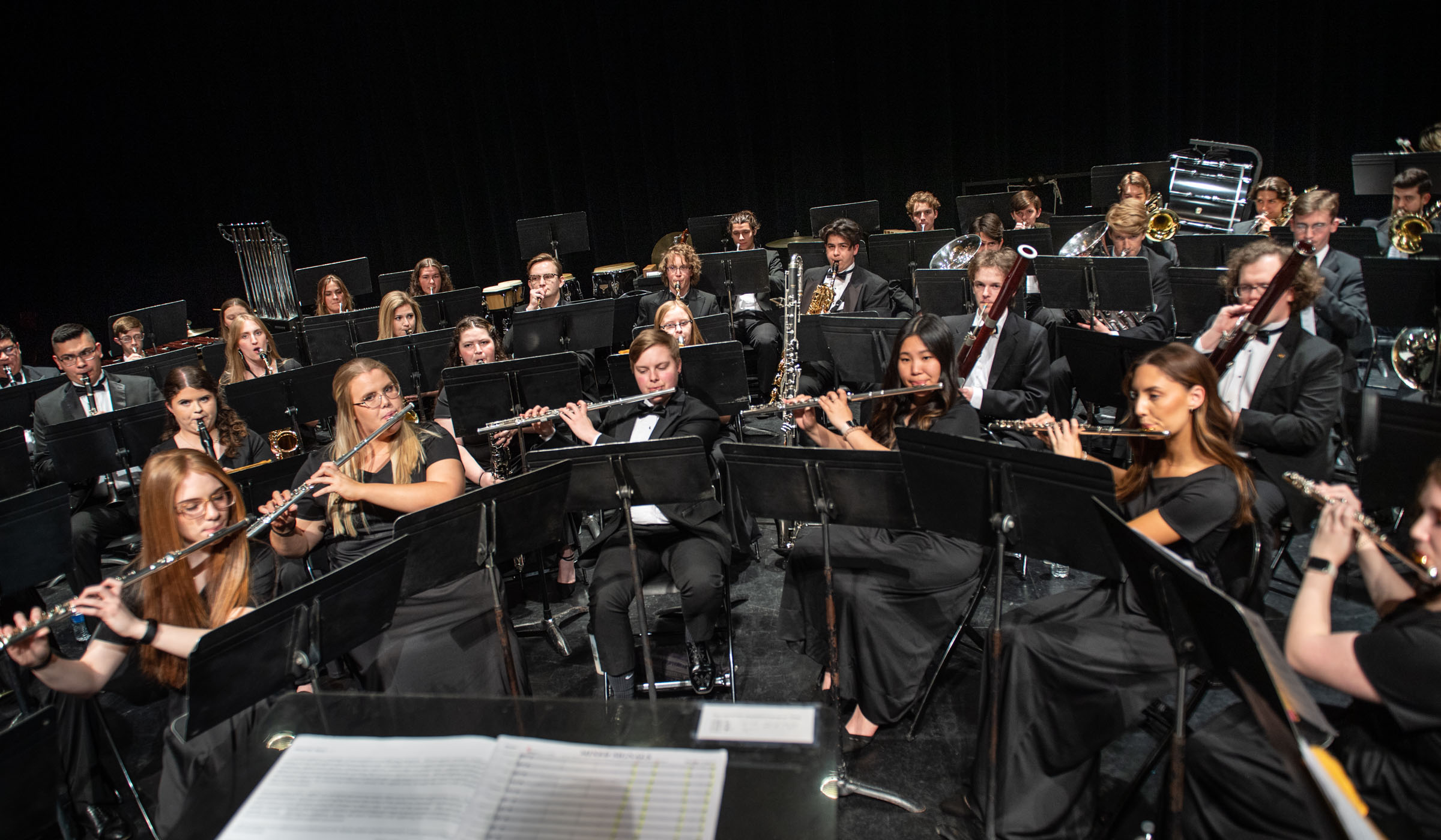 Wide angle of the Wind Ensemble student musicians playing on the stage of Bettersworth Auditorium, taken from the vantage point of the conductor's stand.