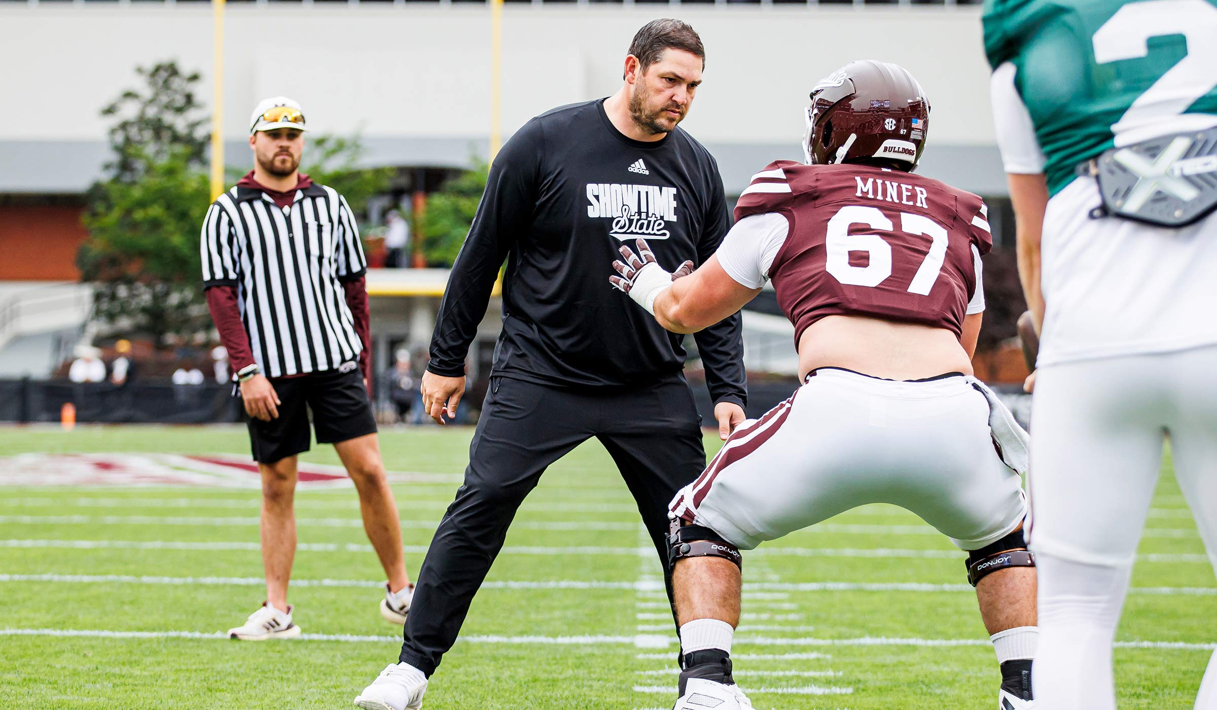 Guy in all black leaning towards guy in maroon and white football uniform on football field