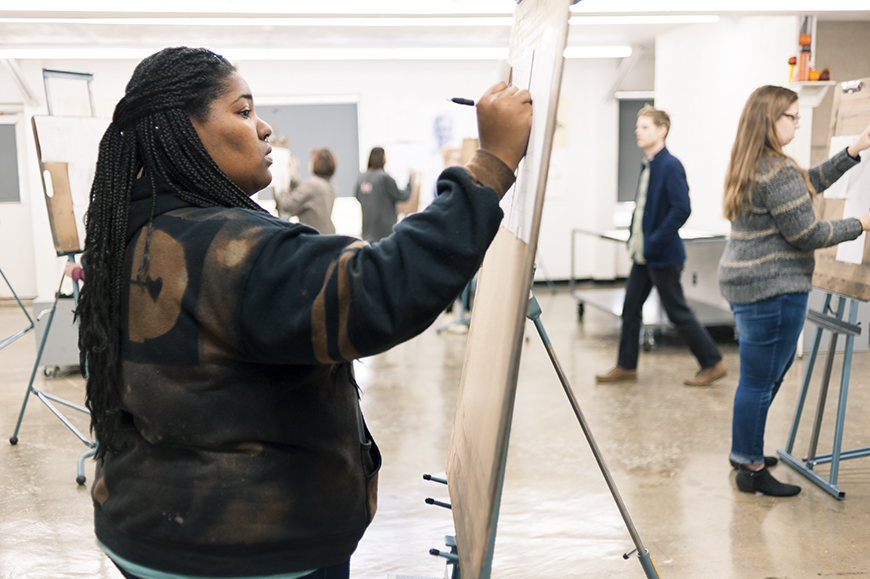 An art students draws on a canvas in a classroom.