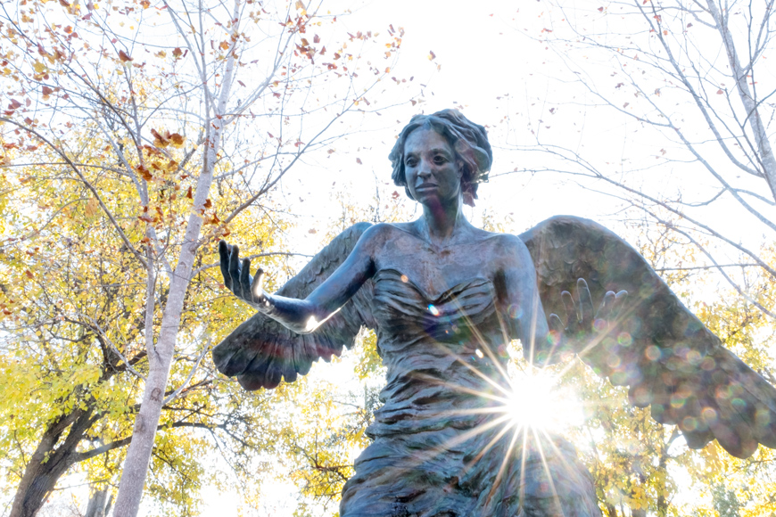 The Chapel's bronze angel sculpture with afternoon sun flare and fall leaves behind