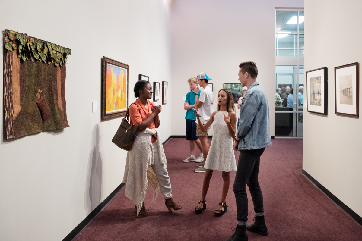 Three students chat in the Cullis Wade Depot Art Gallery, surrounded by art from the Mississippi Museum of Art's collection.