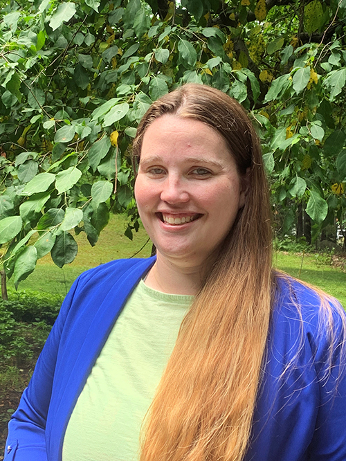Kelsey Slater smiles while standing outside near trees.