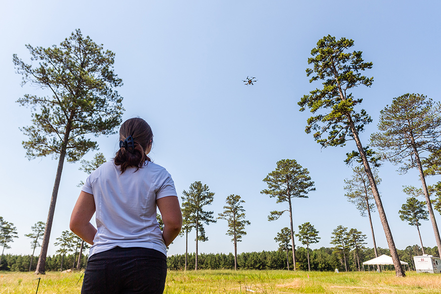 A female student operates a small drone in a forest setting.